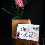 Vase mit Rosenblüte und Grußkarte im Kartenständer