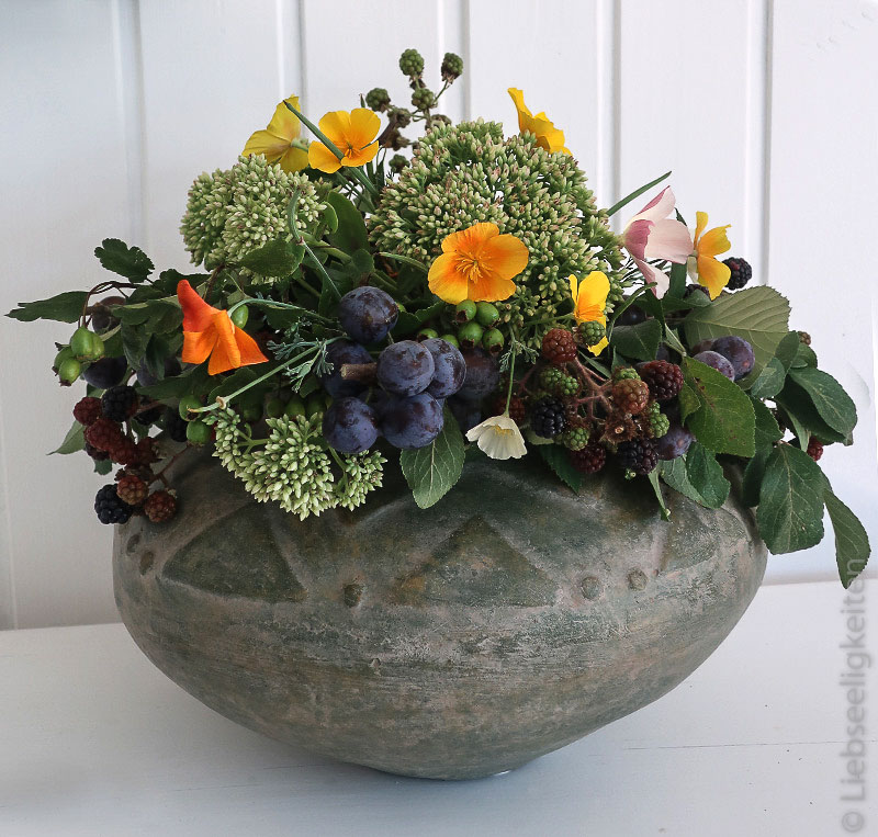 Blumenvase gefüllt mit herbstlichen Blumen und Früchten